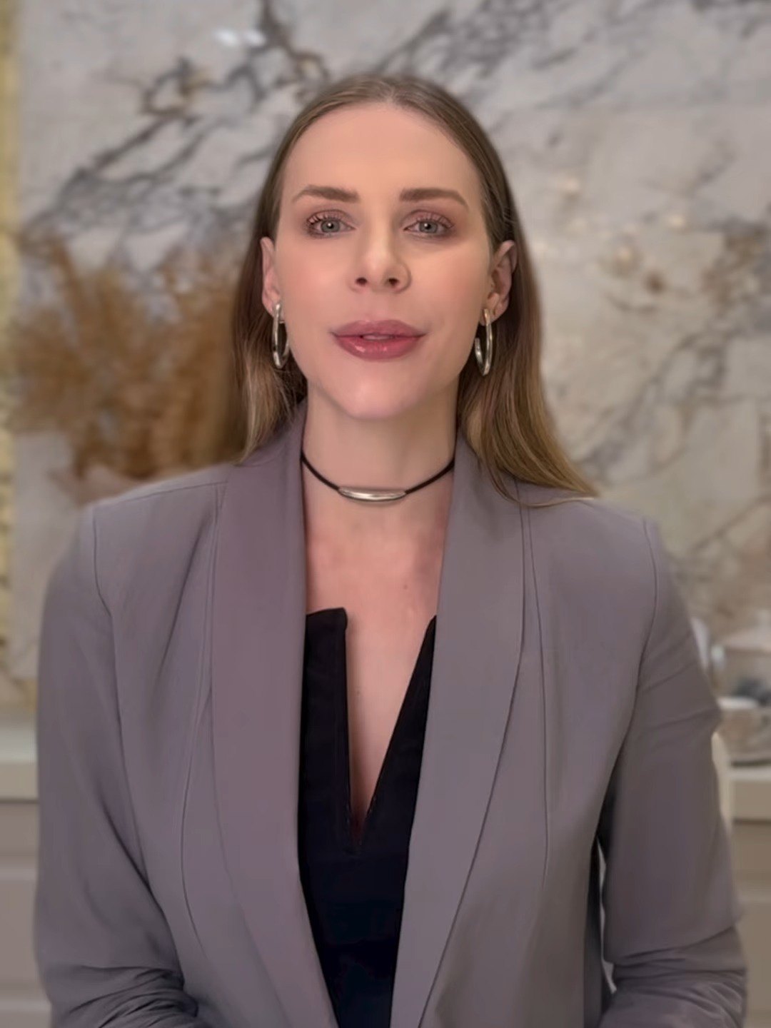 Flávia Calvi, nutricionista, de blazer cinza em frente a uma parede de mármore